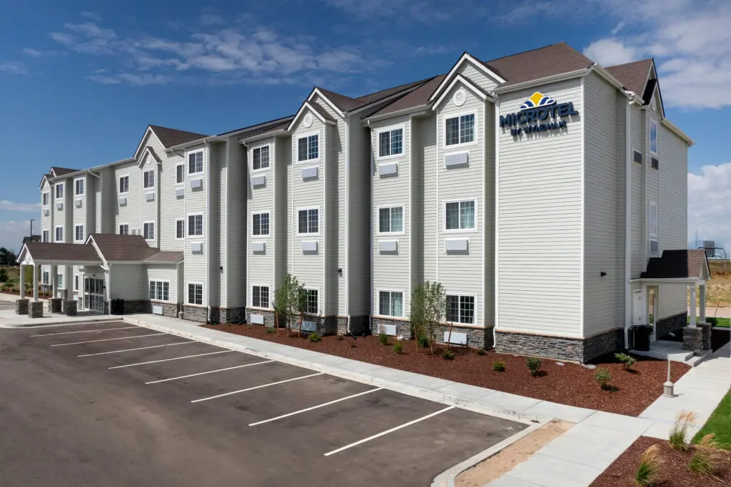 A modern three-story Microtel Inn & Suites hotel with white siding, several windows, a pitched roof, and an empty parking lot in front under a partly cloudy sky.