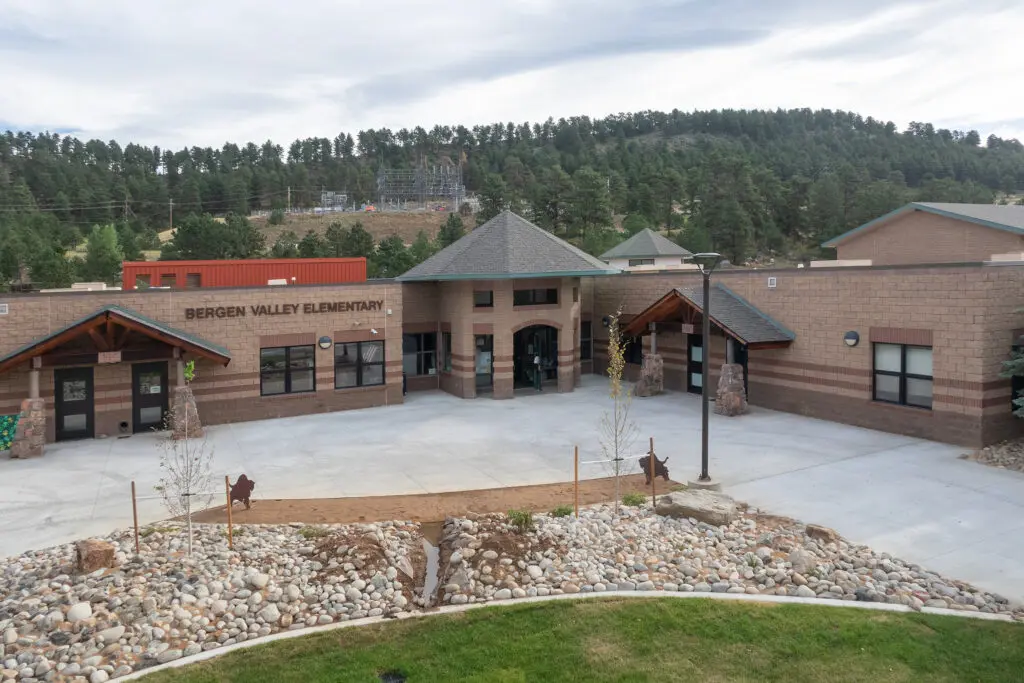 A wide view of Bergen Valley Elementary School, showing a modern brick building with a central entrance, surrounded by rocky landscaping and trees in the background.
