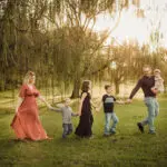 A family holding hands in a field at sunset.