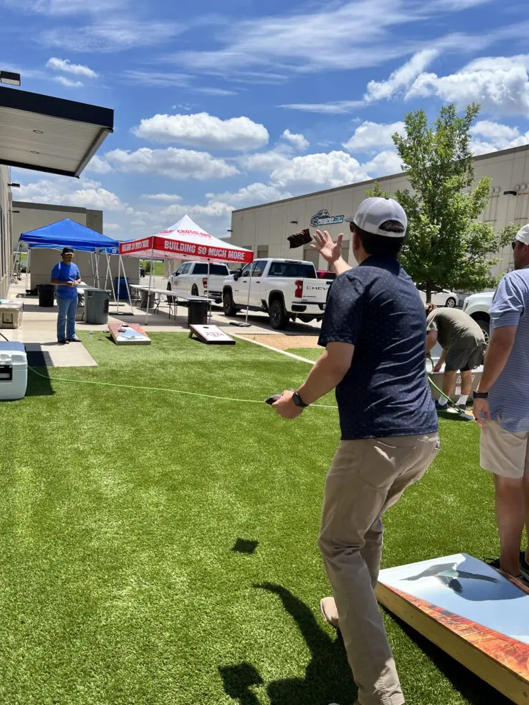 A group of people playing cornhole in a grassy area.