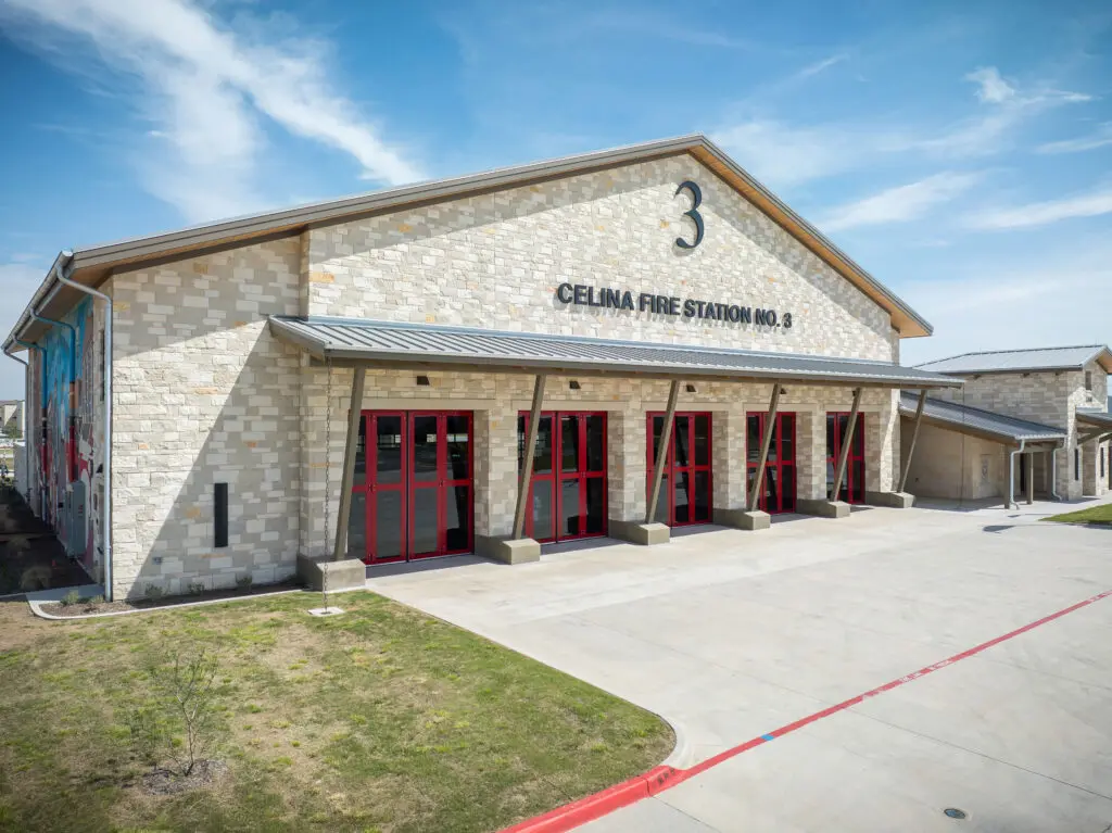 A modern stone building labeled "Celina Fire Station No. 3" with red-framed garage doors and the number 3 displayed above, set under a blue sky with scattered clouds.
