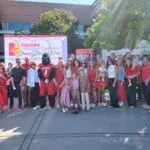 A large group of people, including adults and children, stand together outdoors in front of a "Crossland College of Technology" banner, smiling and posing for a group photo on a sunny day.