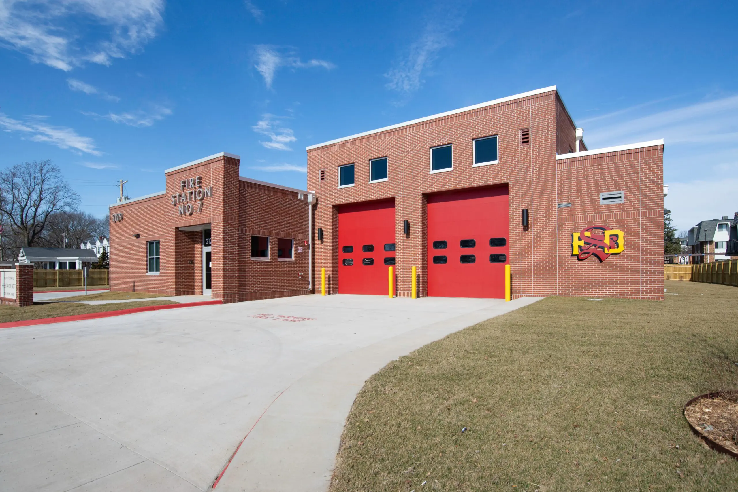 A modern brick fire station with two large red garage doors and a sign that reads “FIRE STATION NO. 1” on the building under a blue sky. There is a paved driveway and grass surrounding the station.