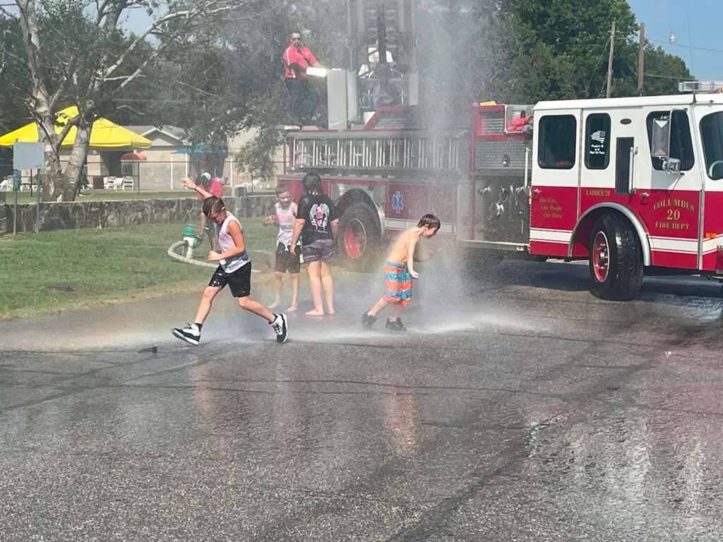 A group of children play in water sprayed from fire engine.