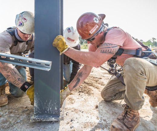 Three construction workers working on a metal pole.