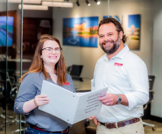 A man and woman standing in an office holding a folder.