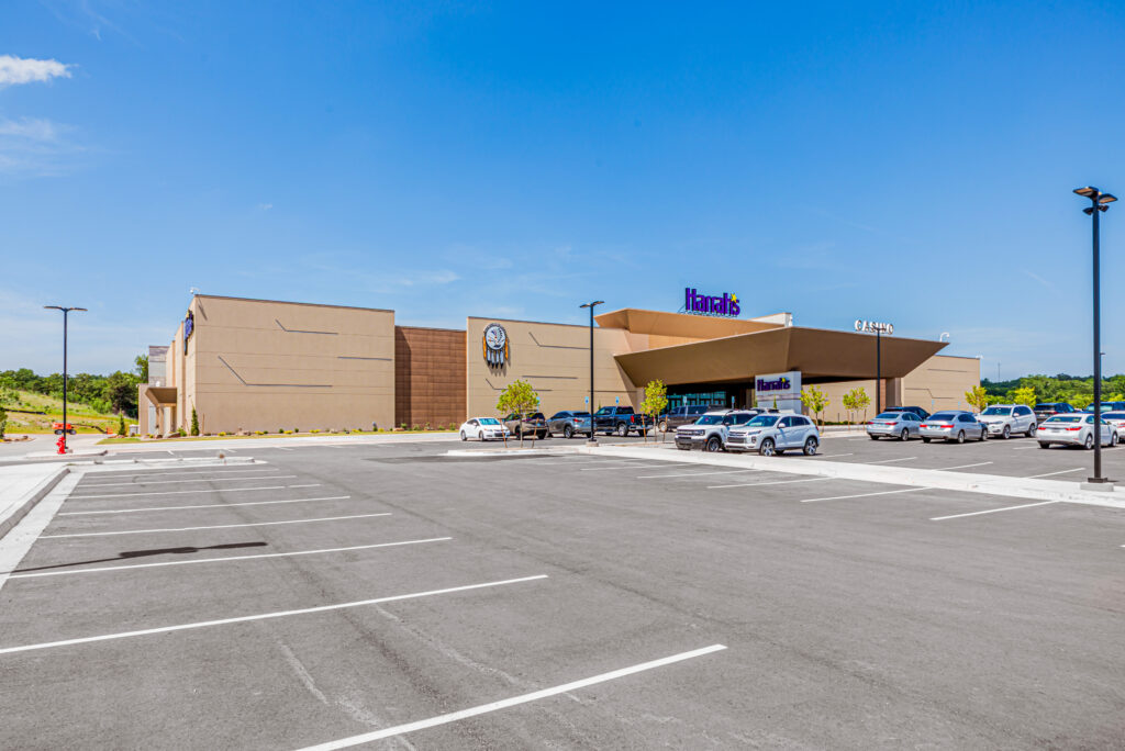 A large retail store with a “JCPenney” sign, a mostly empty parking lot in front, a few parked cars, and clear blue skies above.