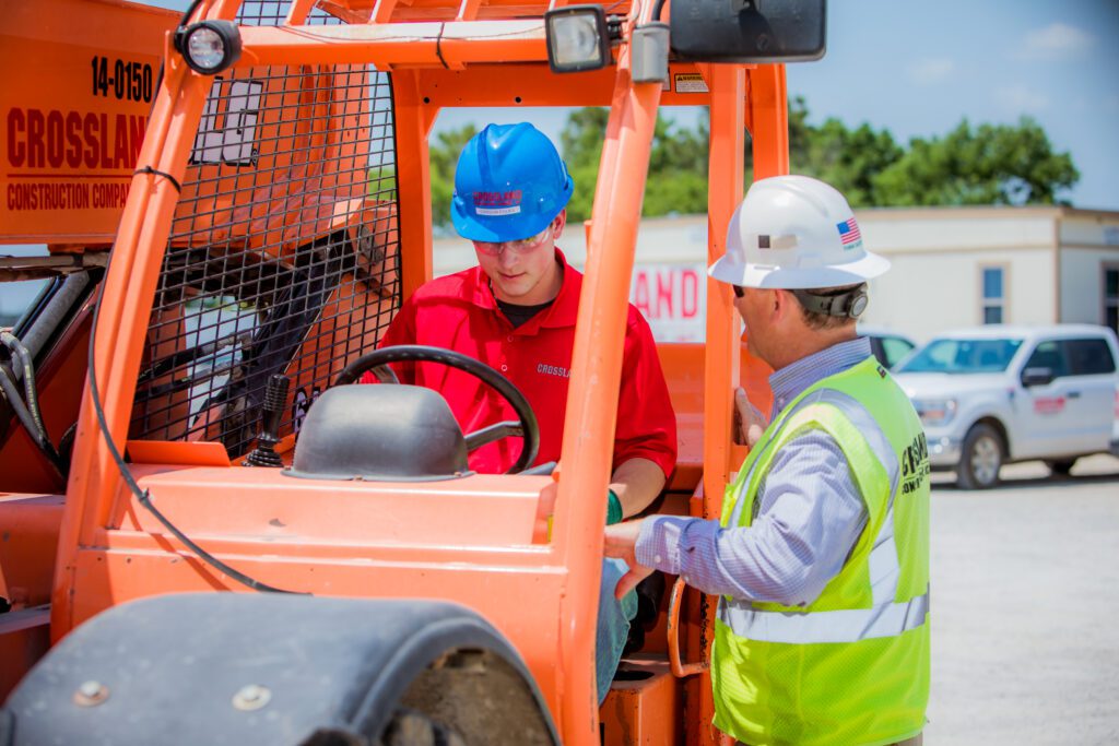 Two men in hard hats standing next to a forklift.