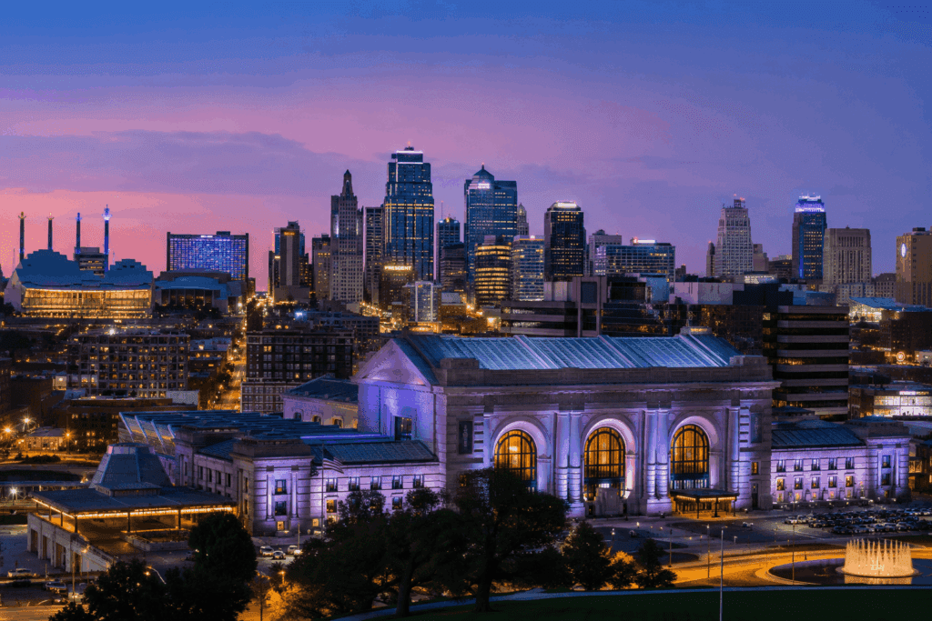 Kansas City skyline at dusk with illuminated Union Station in the foreground, tall buildings in the background, and a colorful purple and pink sky—learn more about Crossland and its impact on this vibrant cityscape.