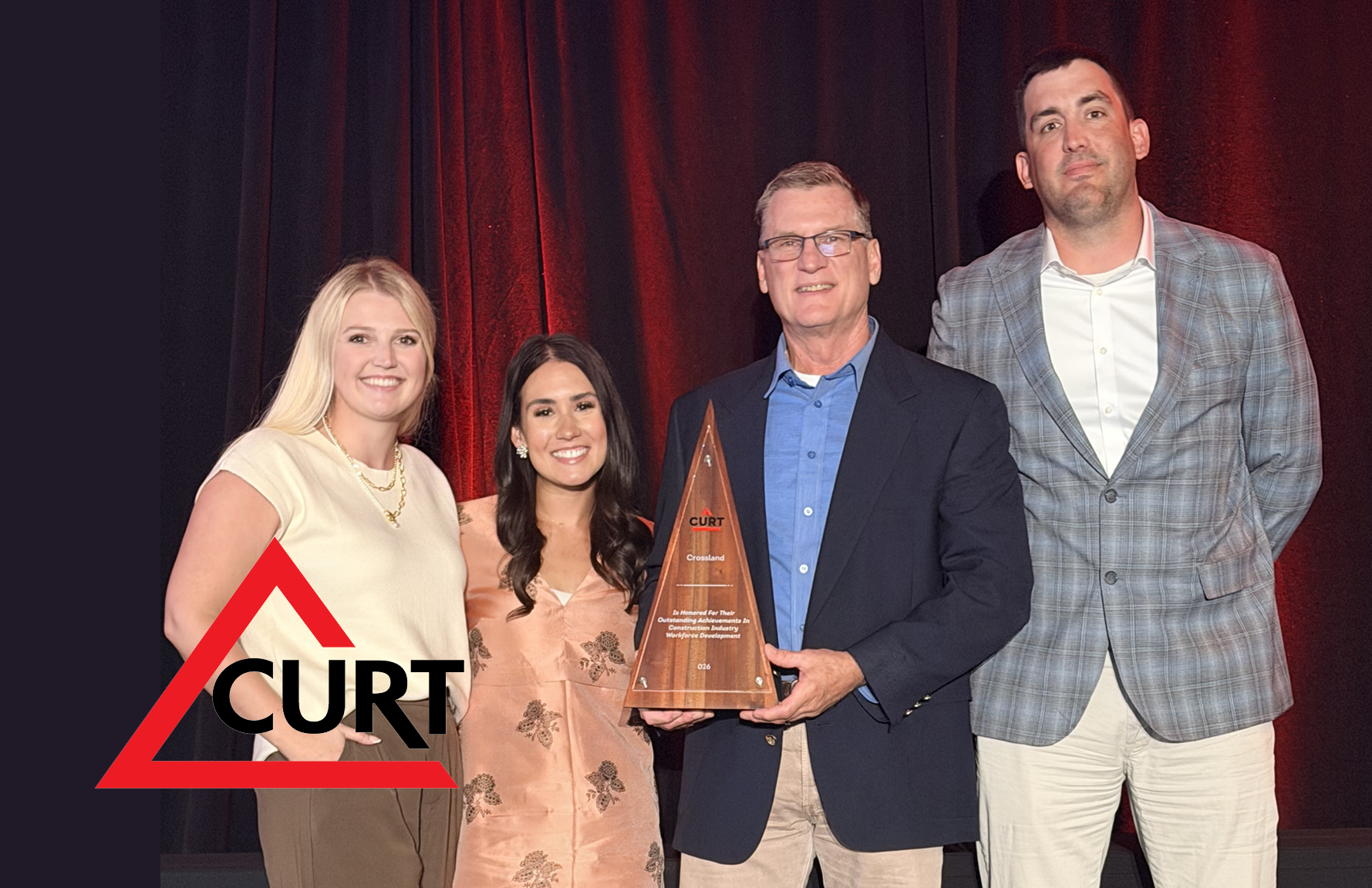 Four people standing together on stage, with the person second from the right holding a triangular award from CURT.