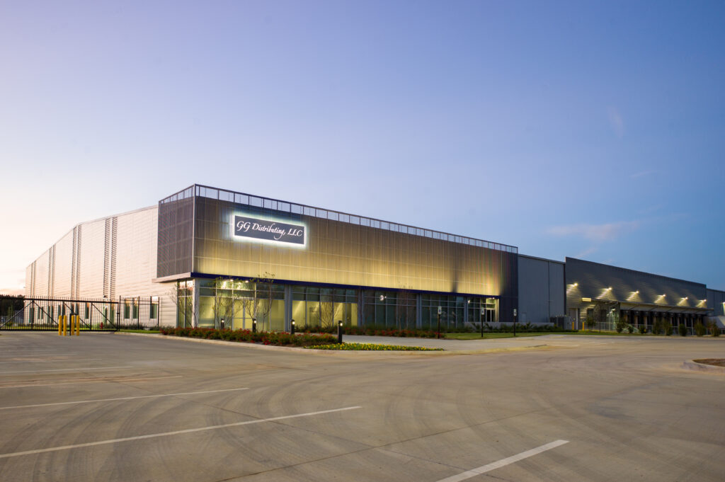 A modern industrial building with a lit sign reading “SGD Drilling, LLC” at dusk, featuring large glass windows, metal panels, and an empty parking lot in the foreground.