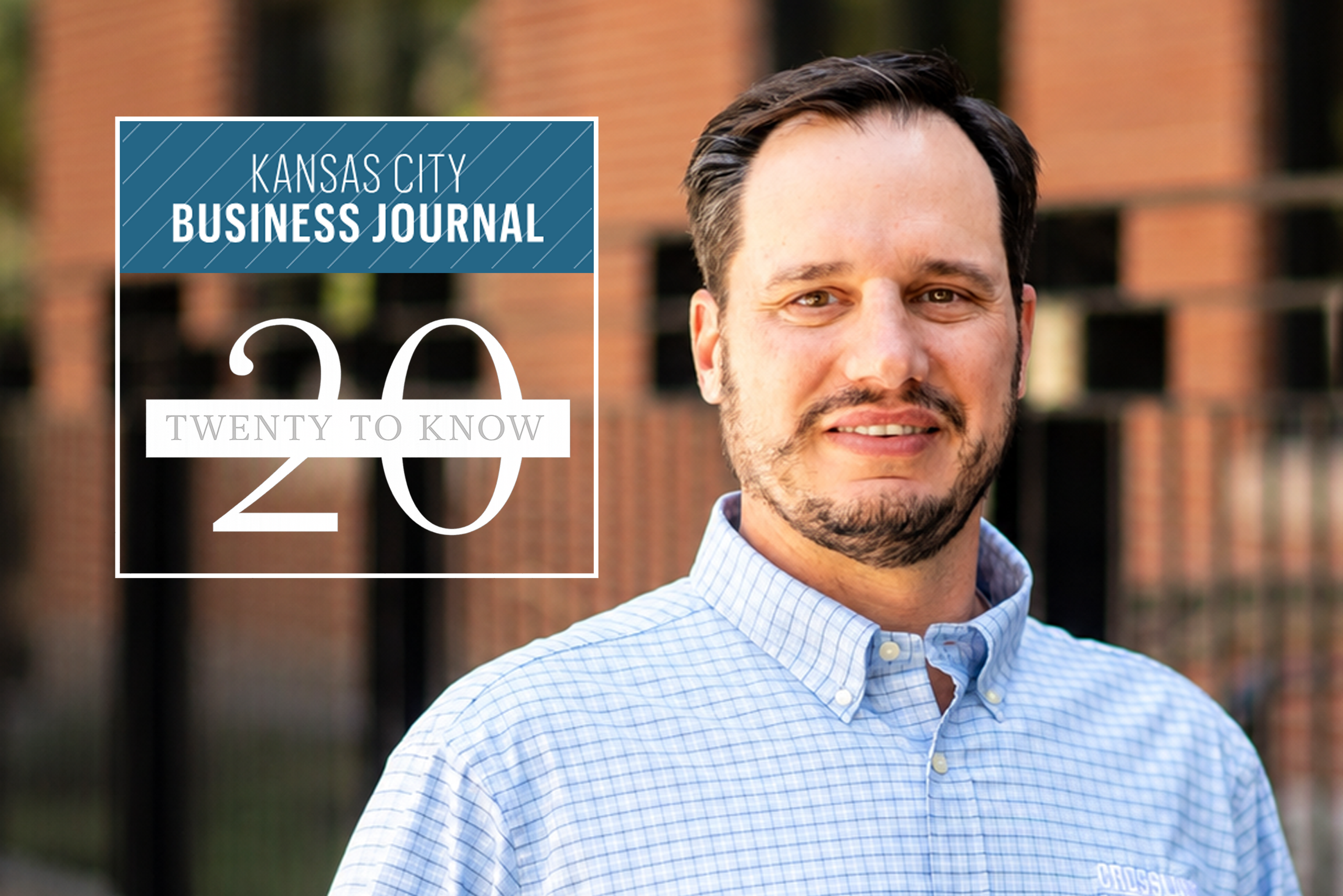 A man in a light blue checkered shirt stands outside. Overlay text reads: “Kansas City Business Journal 20 Twenty to Know.” Brick building and black fence are in the blurred background.