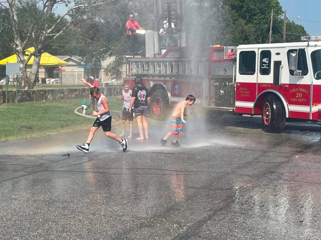 A group of children play in water sprayed from fire engine.