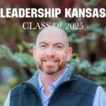 A smiling man with a trimmed beard stands outdoors in front of blurred greenery, wearing a blue checkered shirt and black vest. White text above reads “LEADERSHIP KANSAS CLASS OF 2025.”.