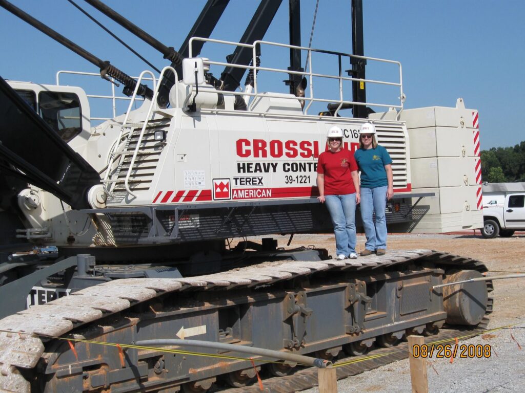 Two people wearing hard hats stand on the tracks of a large white construction crane with "Crosby Heavy Construction" written on its side. The photo was taken outdoors on a sunny day, dated 08/26/2008.