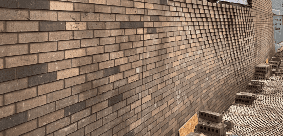 A man is standing on a sidewalk next to a brick wall.