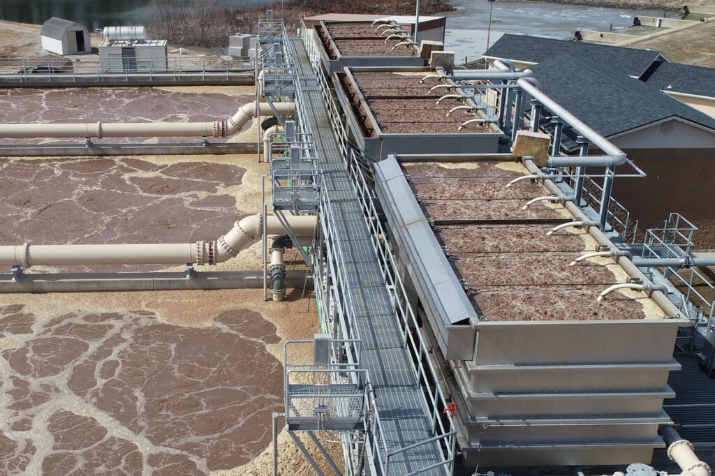 Aerial view of a water treatment facility with tanks of brown liquid, filtration units, and pipes, illustrating the process of wastewater purification outdoors.