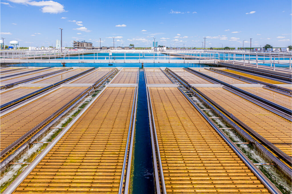 An outdoor water treatment facility with large rectangular basins, metal railings, and clear blue sky with scattered clouds.