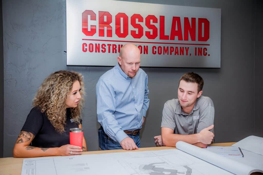 Three Crossland employees reviewing rolled site drawings beneath the Crossland Construction Company sign.