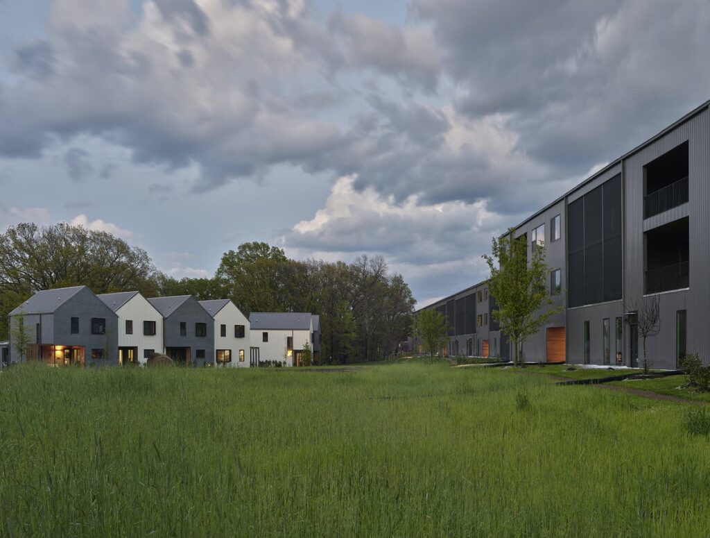 A grassy field with modern homes and buildings in the background.